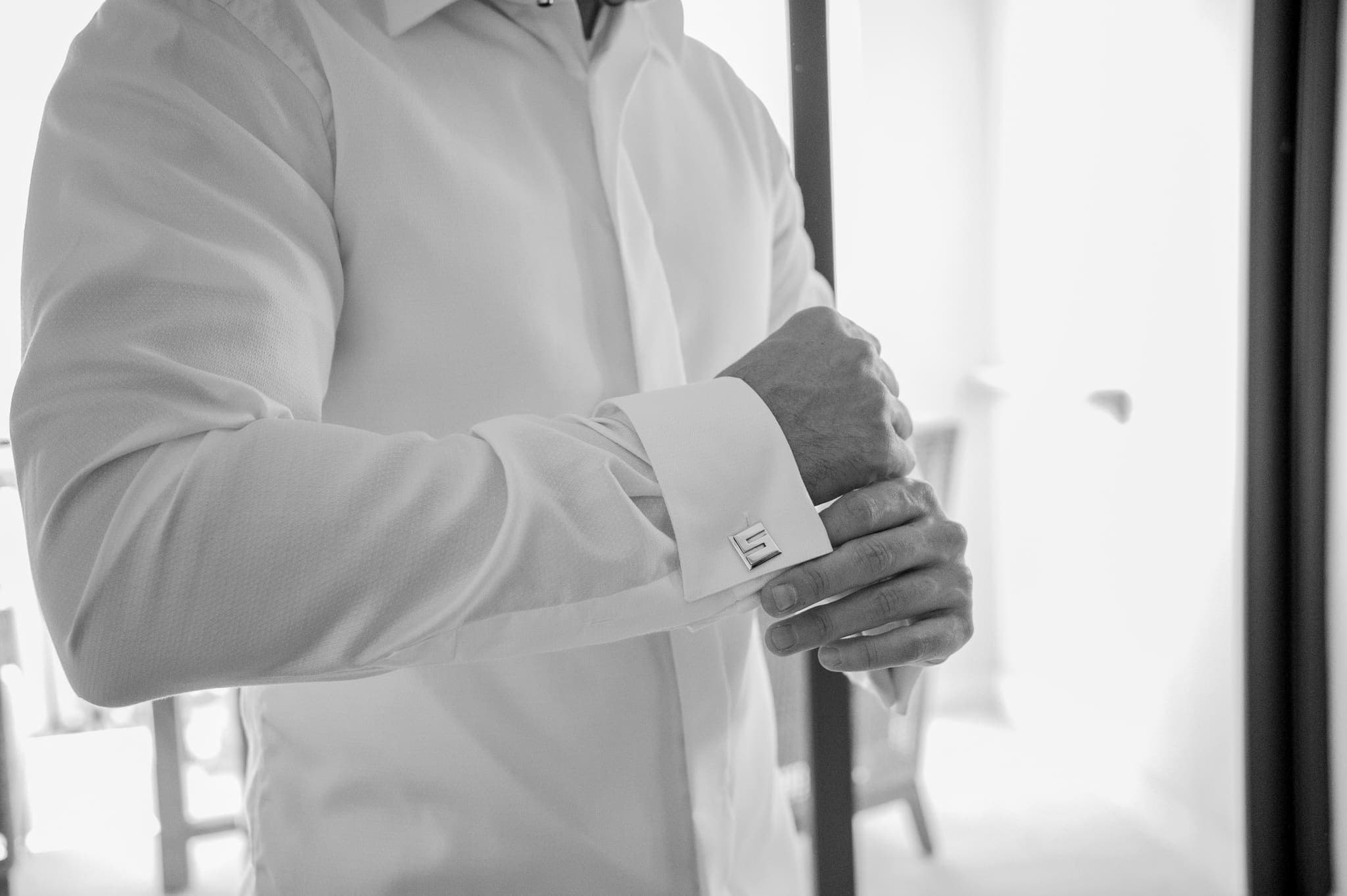 Detalle en blanco y negro del novio abotonando los puños de su camisa