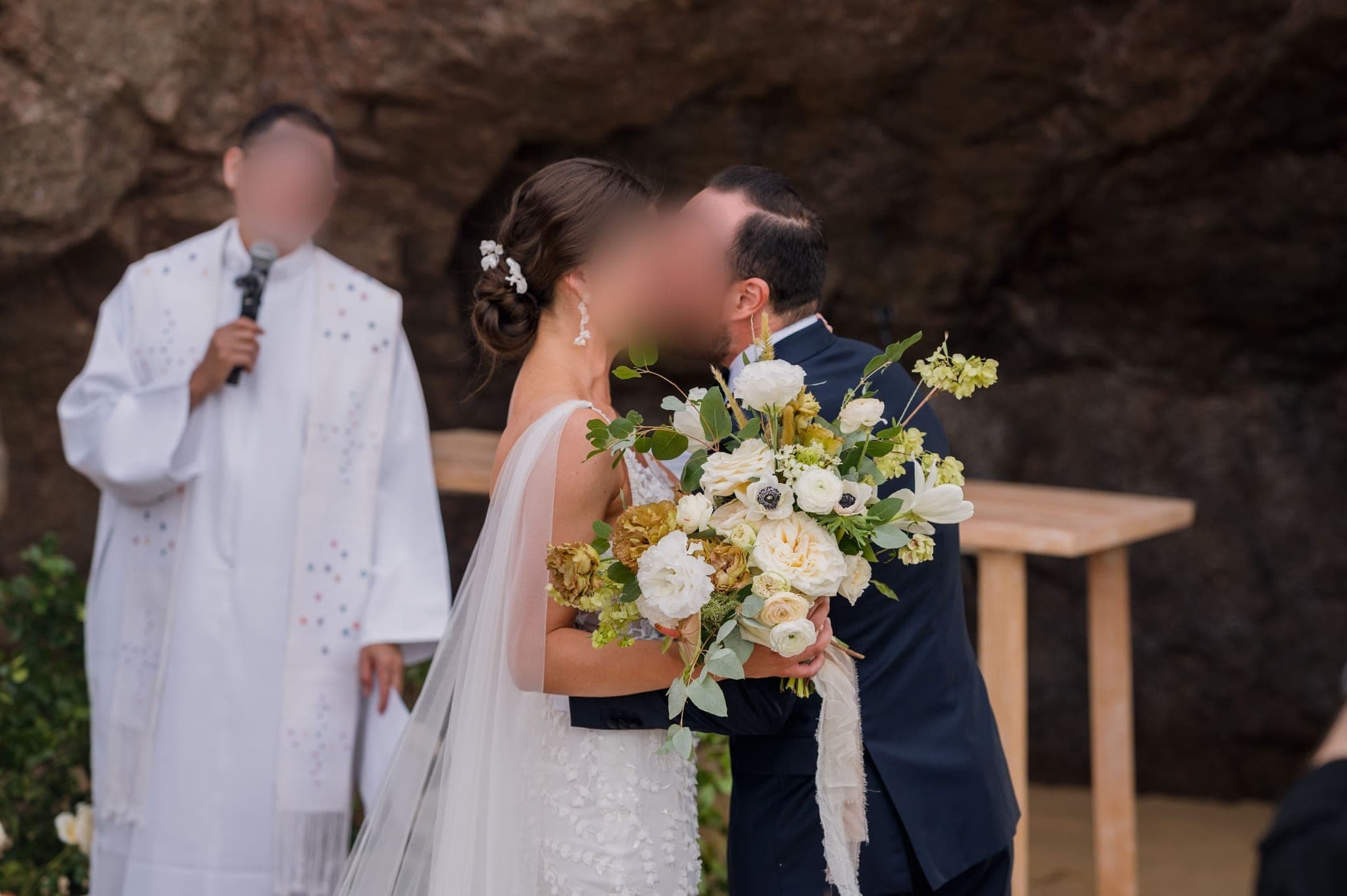 Beso de los novios frente al oficiante, con ramos de flores blancas