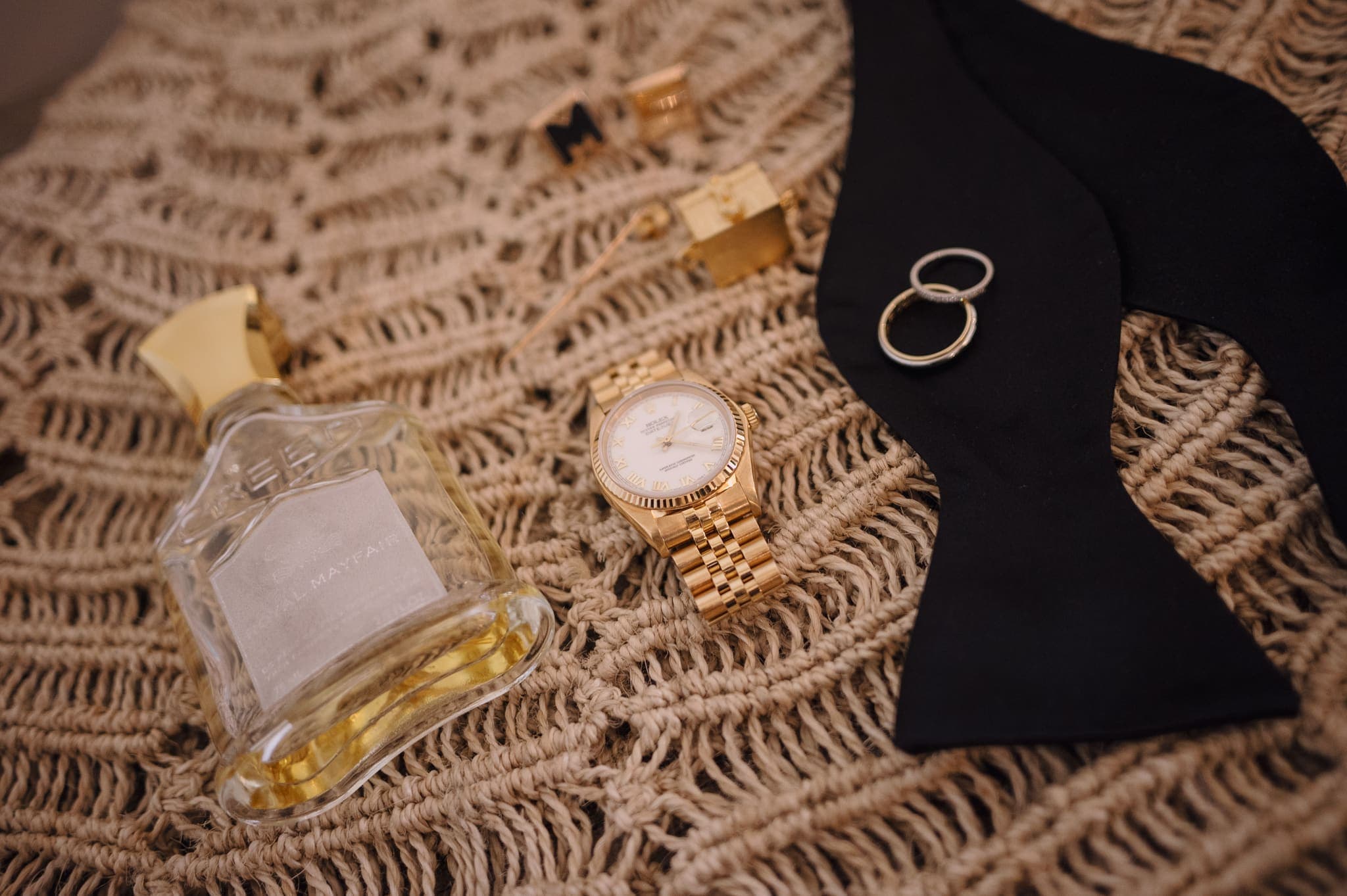 Anillos, reloj y corbatín del novio en composición sobre tejido