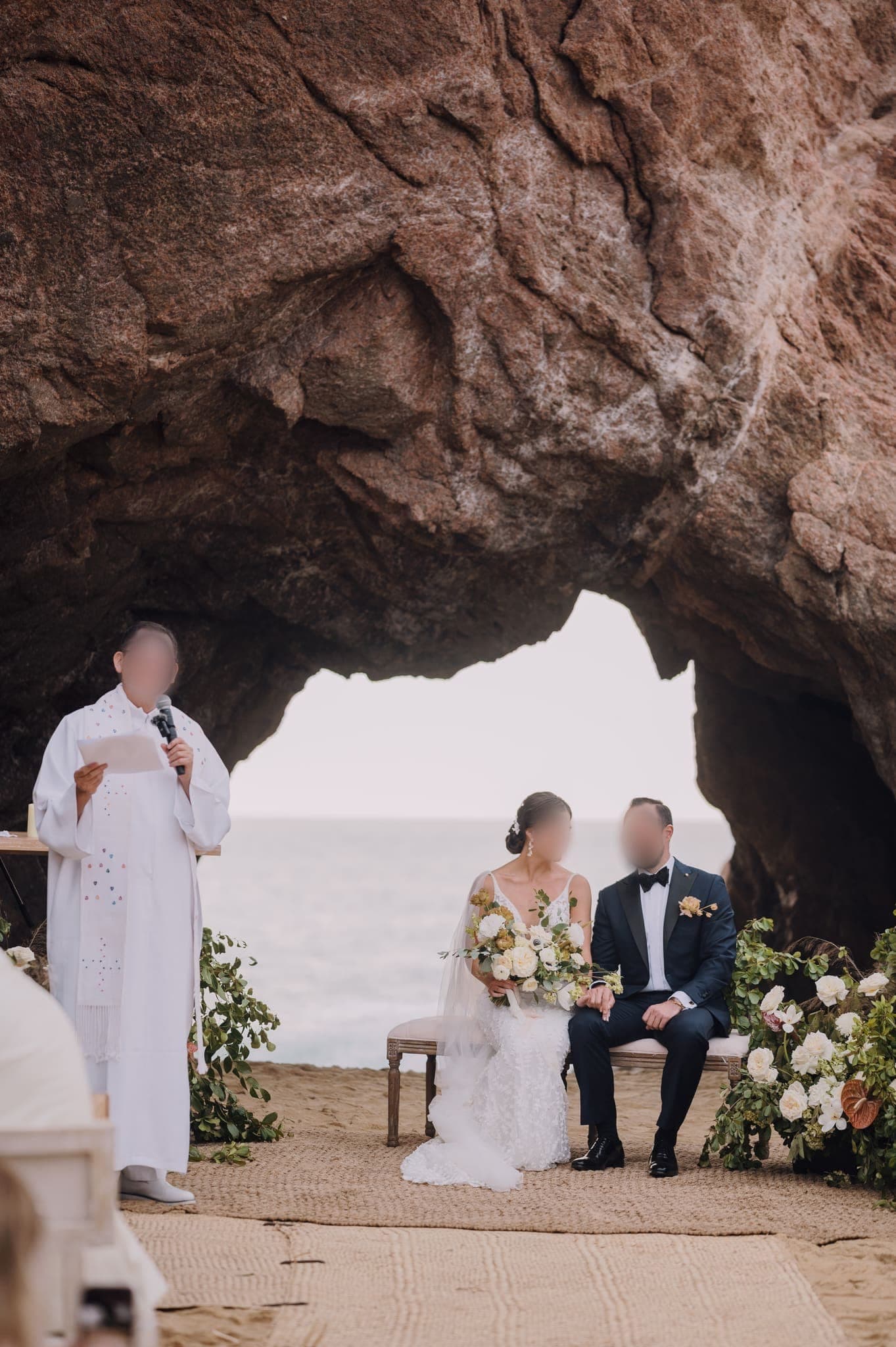 Los novios sentados ante el oficiante bajo el arco de roca