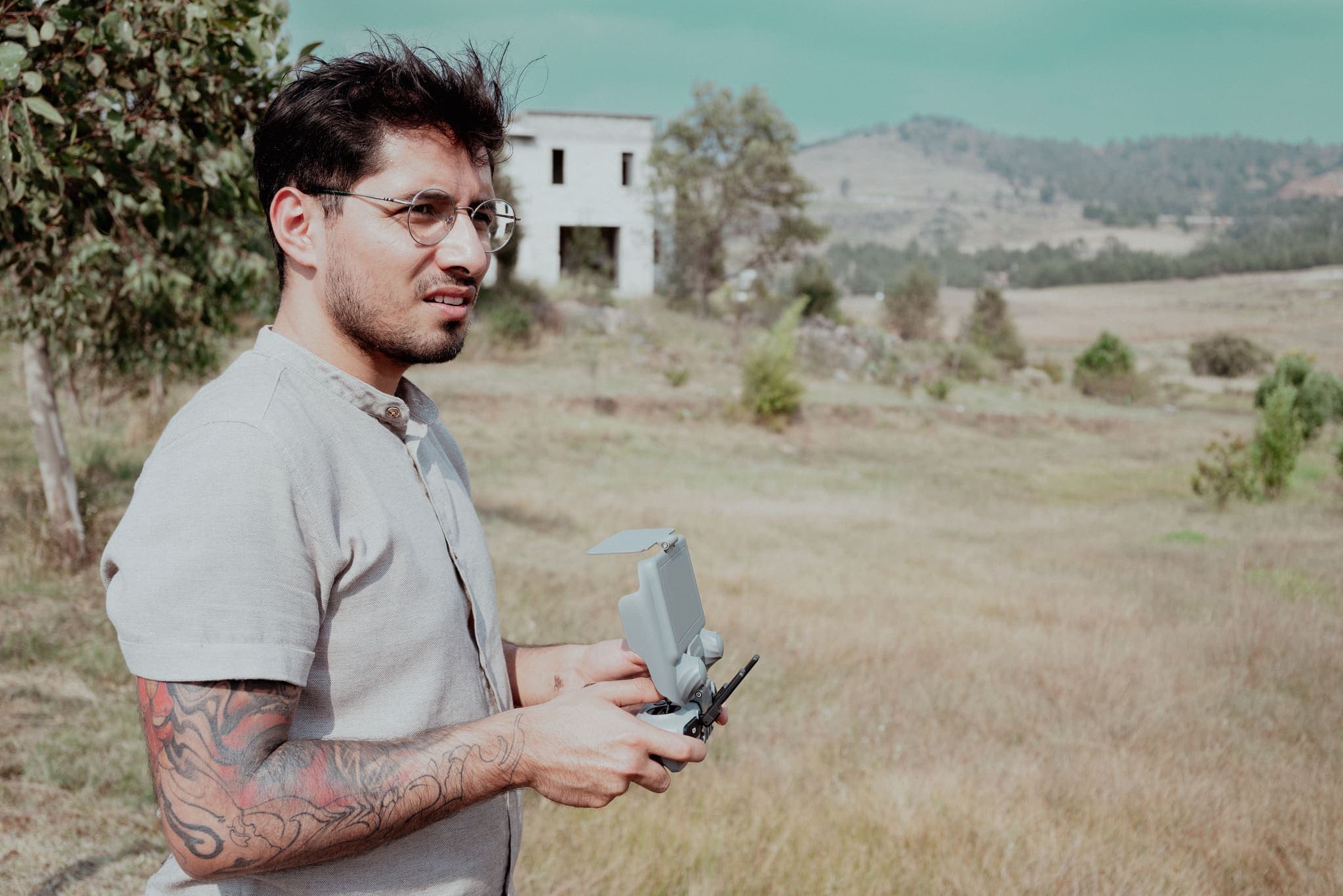 Piloto con el control del dron frente a construcción abandonada en el campo