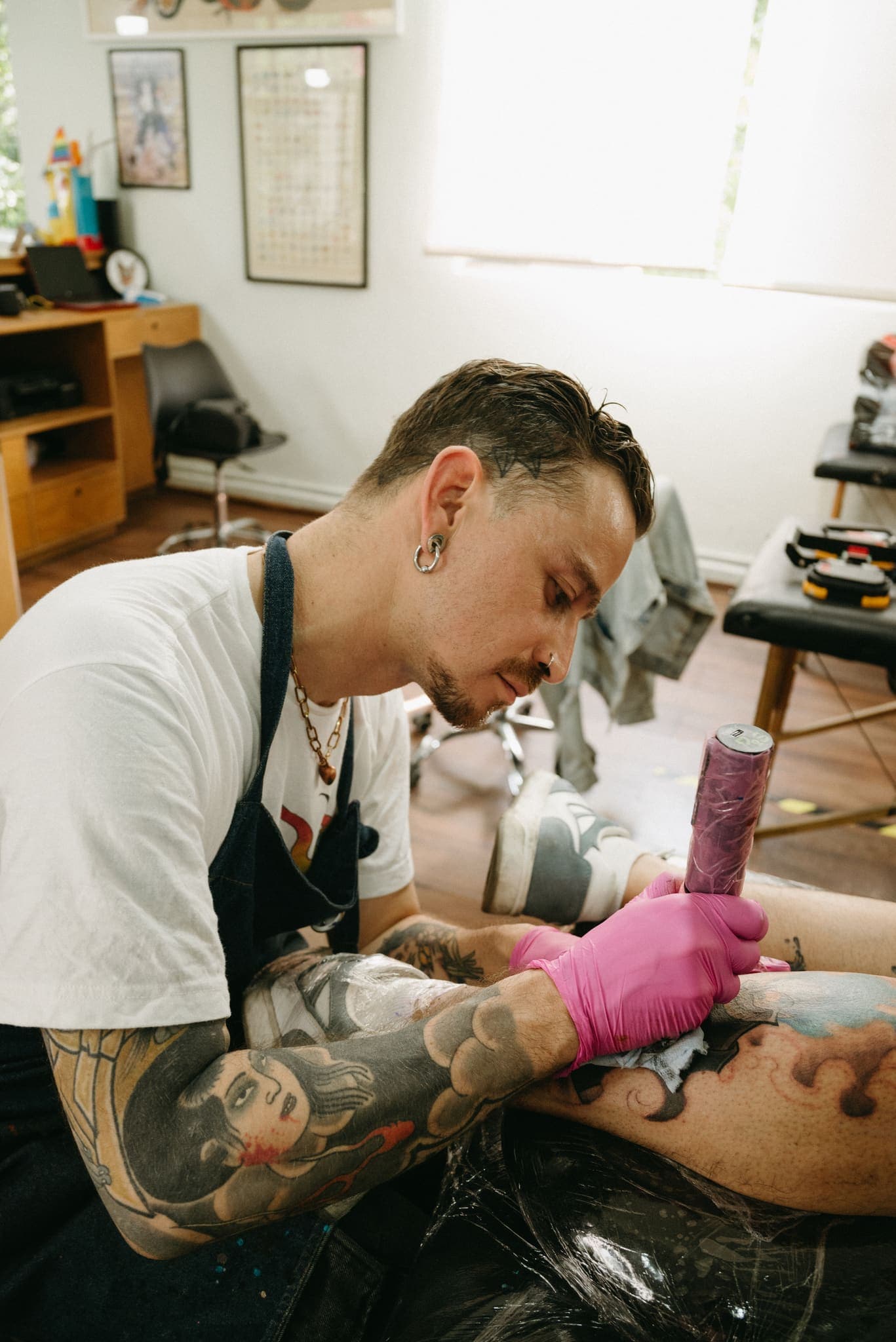 Perfil de tatuador con brazos tatuados aplicando tinta