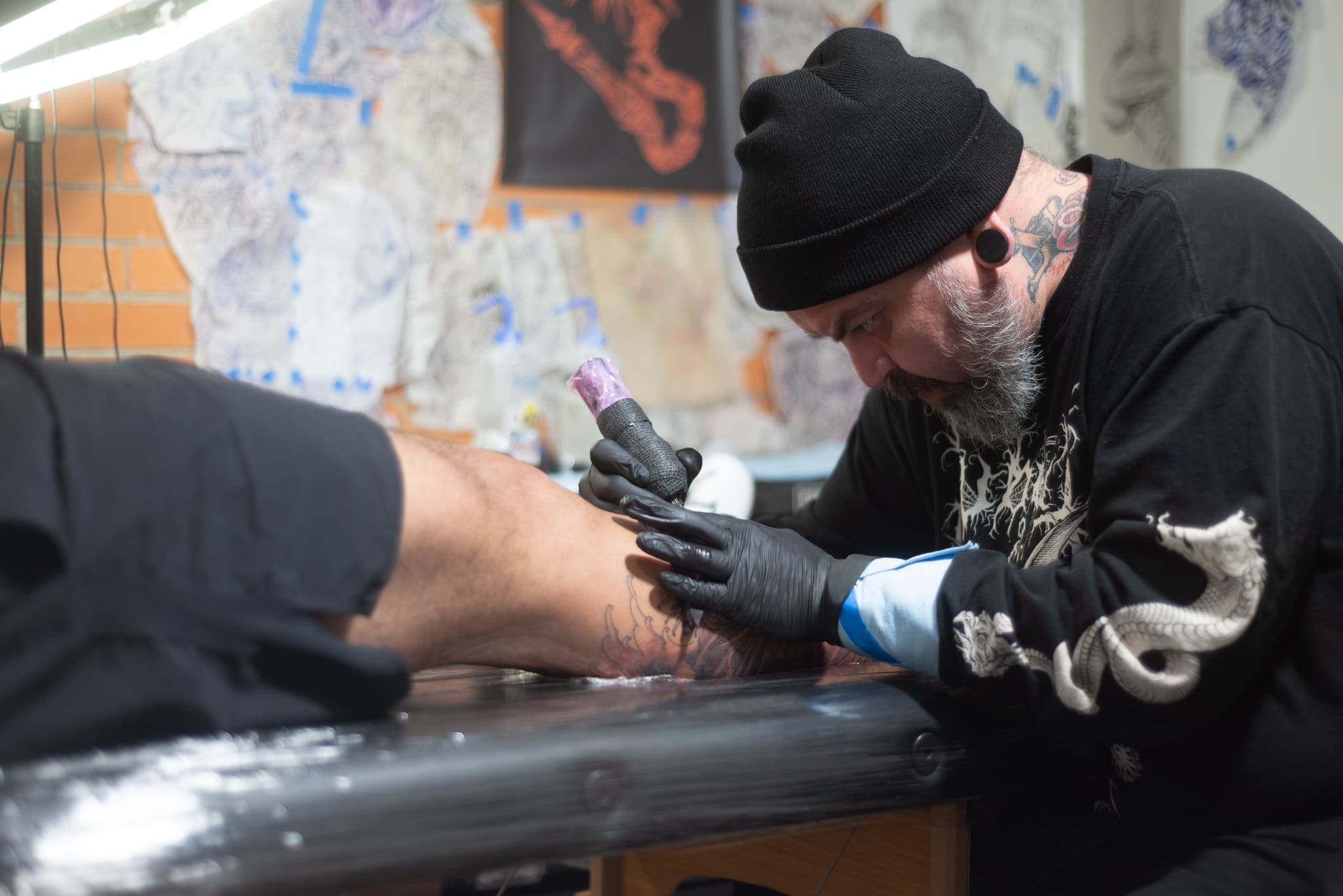 Tatuador trabajando la pierna del cliente en su estudio de ladrillo