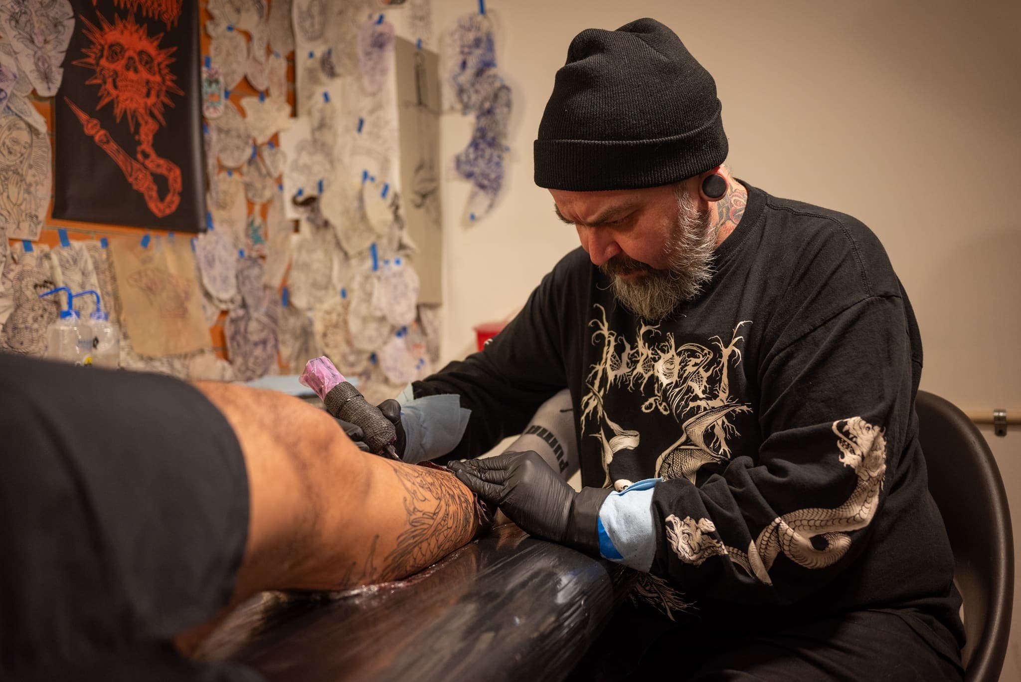 Tatuador inclinado sobre su trazo con la camiseta de diseño gótico