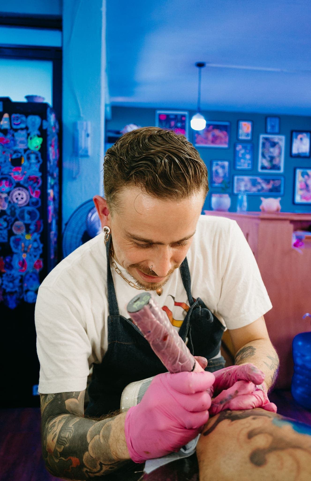 Tatuador aplicando tinta con guantes rosas, estudio en tonos azules