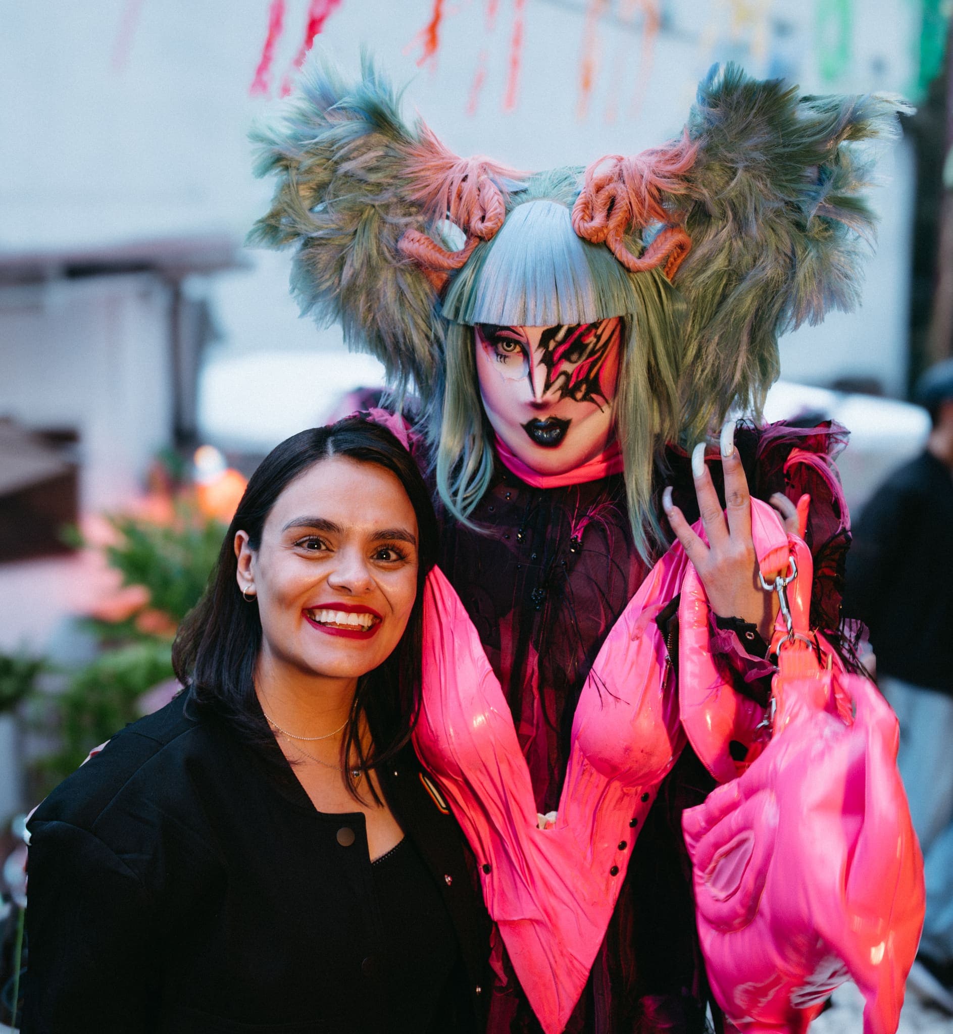 Artista drag y acompañante sonriendo a cámara en exterior