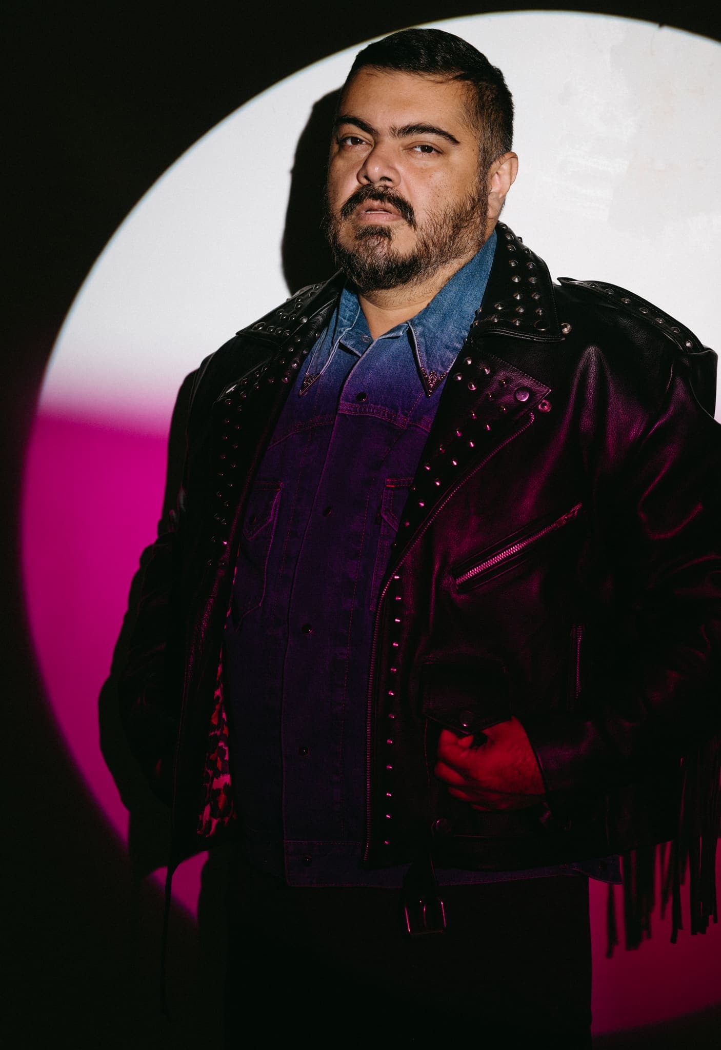 Retrato con chaqueta de cuero y estoperoles bajo círculo de luz rosa